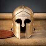 Hand raised brass Greek helmet of the Corinthian hoplite pattern with engraved meander brow band and crest ridge standing on warm sandstone steps