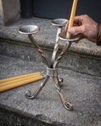Hand setting a beeswax candle onto a pricket of a three branch twisted steel candle holder on a granite step