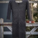 Hand woven chainmail hauberk in blackened mild steel with a four in one butted weave and keyhole neck, hanging on a weathered timber gate in winter light