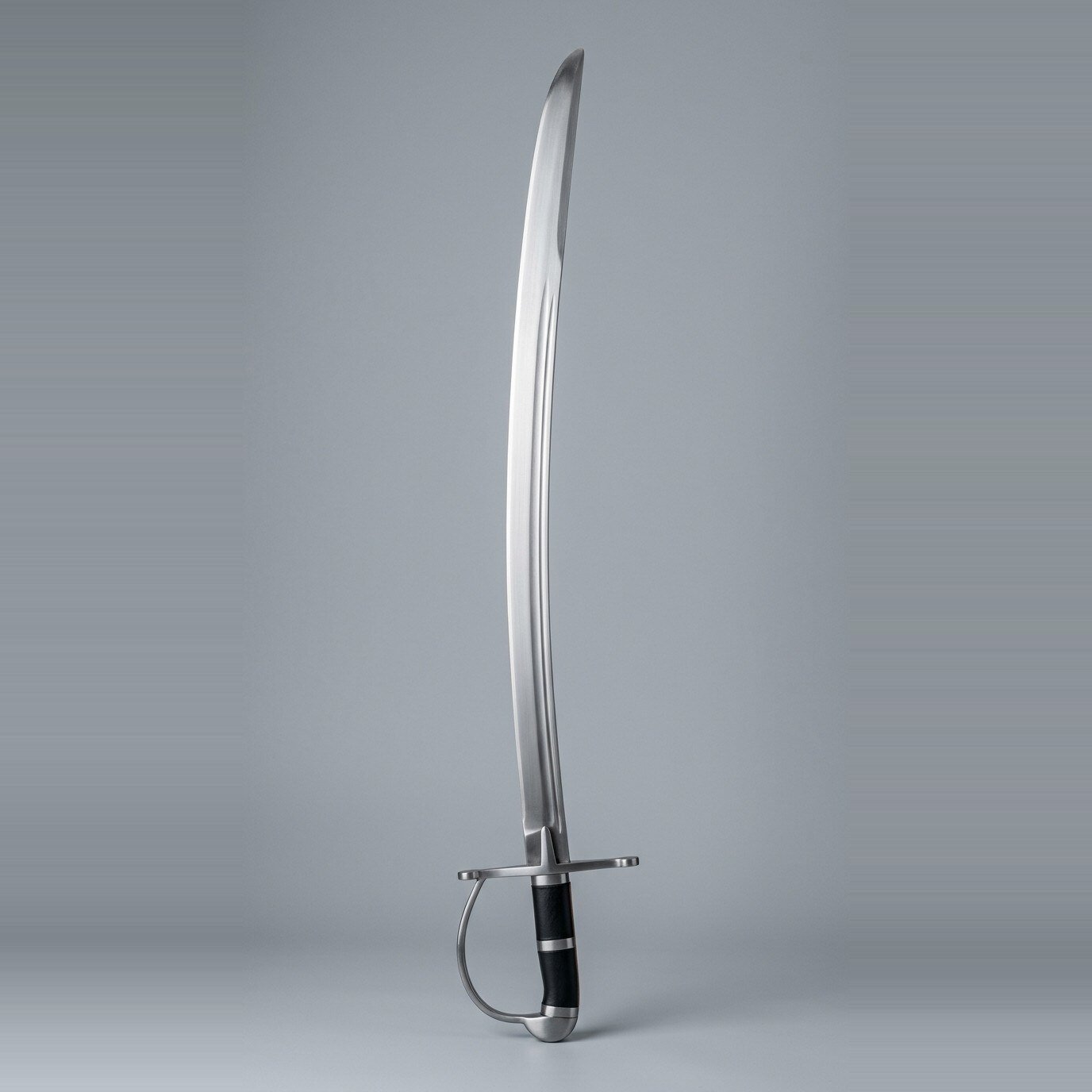Kaldrast hanger sabre trainer RK-3001 Hanger sabre trainer with a curved single edged blunt blade, D shaped knuckle bow and black leather grip laid against a plain studio backdrop
