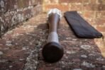 Hardwood baseball bat with engraved knotwork collar and barbed wire wrapped end lying on an old brick wall, zip carry case behind