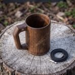 Hardwood Viking beer mug with engraved raven and riveted square handle on a tree stump beside a black leather cord