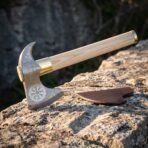 Helm of Awe bearded axe with a pattern welded Damascus head, bright polished eight armed stave, brass collar, pale ash haft and brown leather cover on a sunlit rock