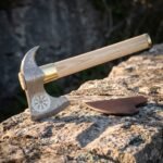 Helm of Awe bearded axe with a pattern welded Damascus head, bright polished eight armed stave, brass collar, pale ash haft and brown leather cover on a sunlit rock
