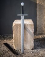 Helm of awe damascus sword with an engraved Aegishjalmur stave below a wide flat guard, black leather grip and bossed wheel pommel standing against a cut stone block