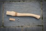 Hickory axe haft with carved Celtic knot band laid on slate paving next to a wooden wedge and two steel ring wedges