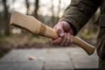 Hickory axe haft with a carved Celtic knotwork band held in one hand outdoors, showing the kerfed eye end