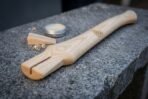 Hickory axe handle with a slotted eye and valknut engraving on granite, wooden wedge, curled shavings and a wax tin behind