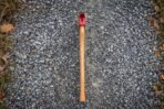 Hickory handled felling axe with red painted head laid straight on grey gravel, seen from directly above