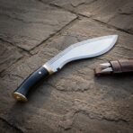 High carbon kukri with black horn handle and brass butt cap, handle in the foreground and rune band along the spine on paving