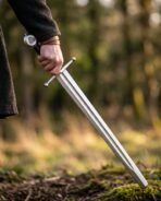 High carbon steel arming sword with ball tipped crossguard and Valknut pommel held point down above mossy ground