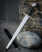 High carbon steel arming sword with rune column etched in the fuller propped on a rock next to its black scabbard