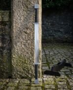 High carbon steel double ended sword standing upright against a granite pillar with its wooden stand beside it