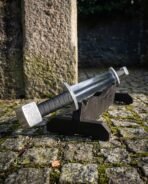 High carbon steel double ended sword with knotwork block pommel, close up angled on its wooden stand on cobbles