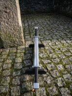 High carbon steel double ended sword with twin cord wrapped grips resting on a dark wooden stand on cobblestones