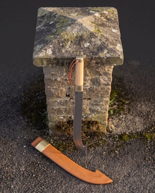 Hooked Damascus sabre hanging by its leather lanyard from a mossy stone post with the tan leather scabbard below