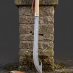 Hooked damascus sabre with a deeply curved pattern welded blade, pale hardwood grip and brass ferrule standing against a dry stone gatepost