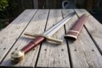 Knightly sword with brass fittings and burgundy grip on a garden table beside its matching burgundy scabbard