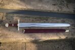 Knightly sword with brass guard and pommel, oxblood leather grip and matching scabbard with brass chape on stone steps