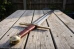 Knightly sword with brass guard, brass wheel pommel and burgundy leather grip lying on a weathered garden table