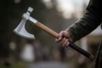 Knotwork engraved bearded axe with hammer poll and steel collar held out in one hand on a woodland path