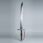 Kriegsmesser trainer with a curved clipped point blade, knuckle bow, walnut scales on five brass rivets and a trumpet butt cap standing point up against a plain grey studio backdrop