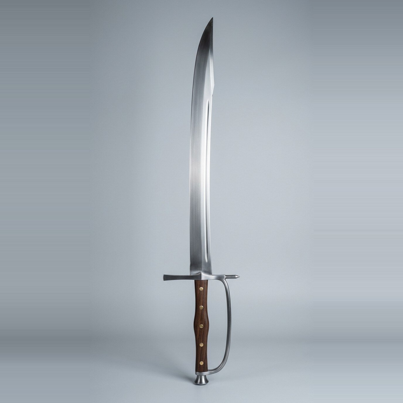 Storvekk kriegsmesser trainer Kriegsmesser trainer with a curved clipped point blade, knuckle bow, walnut scales on five brass rivets and a trumpet butt cap standing point up against a plain grey studio backdrop