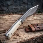 Kukri knife with bone handle scales and steel cap, close up of the handle in front with the blade rising over a log