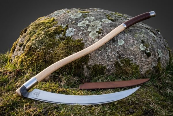 Long ash hafted war scythe with a sweeping polished steel blade and triquetra etching leaning against a lichen covered boulder on open grass