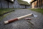 Long Damascus steel bearded axe with ash haft and leather wrapped butt laid on a gravel path between turf roofed houses
