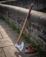 Long handled viking axe with a polished bearded head engraved with a Vegvisir, leather wrapped haft, leaning on a stone parapet beside a fitted leather blade cover
