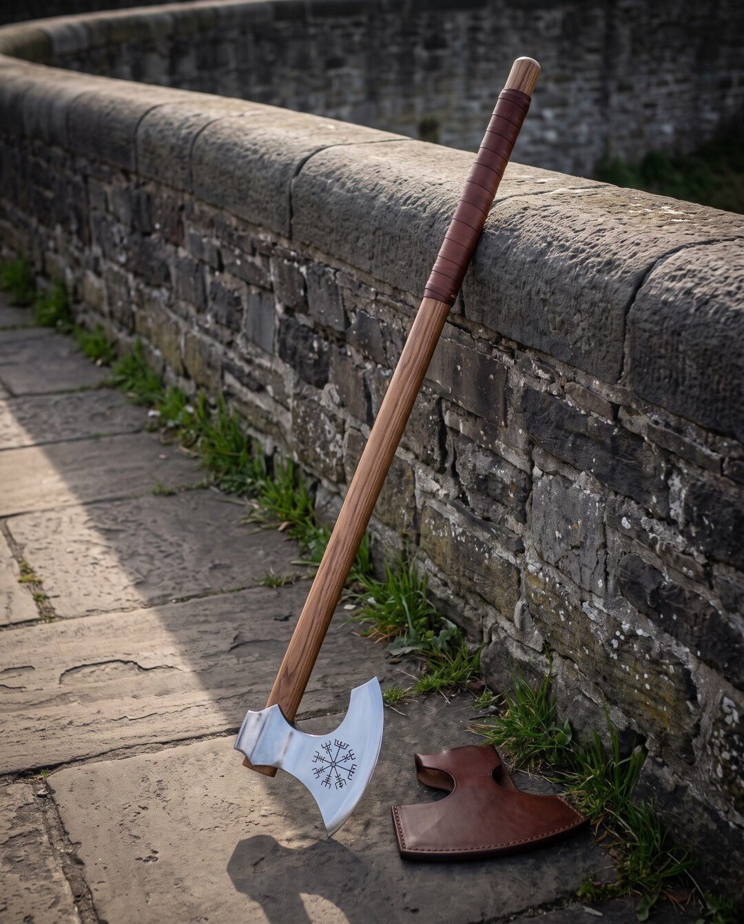 Long handled viking axe with a polished bearded head engraved with a Vegvisir, leather wrapped haft, leaning on a stone Long handled viking axe with a polished bearded head engraved with a Vegvisir, leather wrapped haft, leaning on a stone parapet beside a fitted leather blade cover