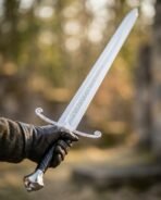 Longsword with etched knotwork blade, scrolled cross guard and black leather grip held up in a gloved hand