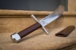 Low angle view of a falchion hilt with steel pommel, brown leather grip and valknut engraving on sandstone