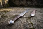 Low angle view of a steel wheel pommel and brown leather grip on a pattern welded arming sword lying on stone paving
