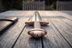 Low close view of a bronze toned lobed pommel, wire wrapped grip and straight guard of a Damascus sword on a wooden table