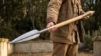 Man holding a Viking spear with leaf shaped steel head forward on a pale ash haft in a walled garden