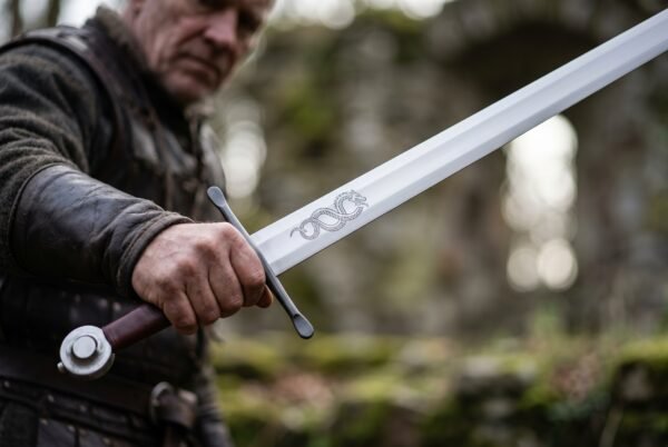 Man in leather armour holding out a serpent etched display sword with a wheel pommel in front of ruined stone walls
