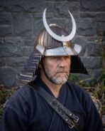 Man wearing a steel kabuto helmet with crescent crest and rune cut brow band in front of a stone wall