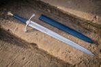 Medieval longsword with blue grip and brass pommel lying next to its blue leather scabbard on a stone step