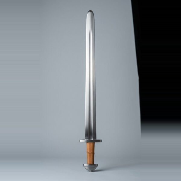 Migration era arming sword with a broad shallow fuller, two part pommel and tan leather grip standing point up against a plain grey studio backdrop