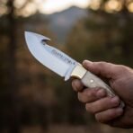 Mirror polished carbon steel gut hook knife with stag antler handle, brass bolster and etched runes held in a hand