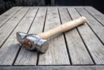 Mirror polished cross pein hammer head with engraved knotwork band and wooden wedge on a weathered table