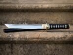 Mirror polished tanto blade with a visible shinogi ridge and a brass collar engraved with interlaced knotwork