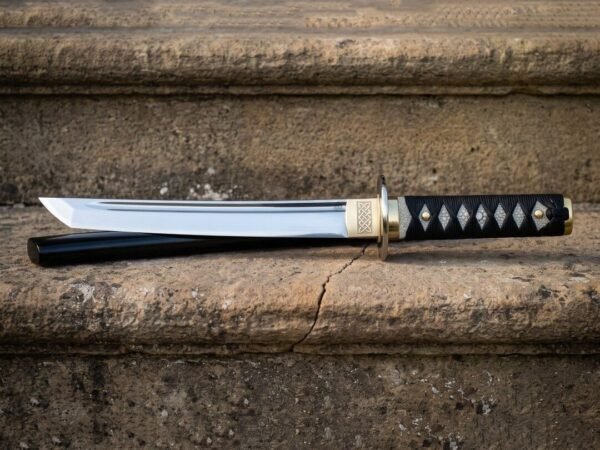 Mirror polished tanto blade with a visible shinogi ridge and a brass collar engraved with interlaced knotwork