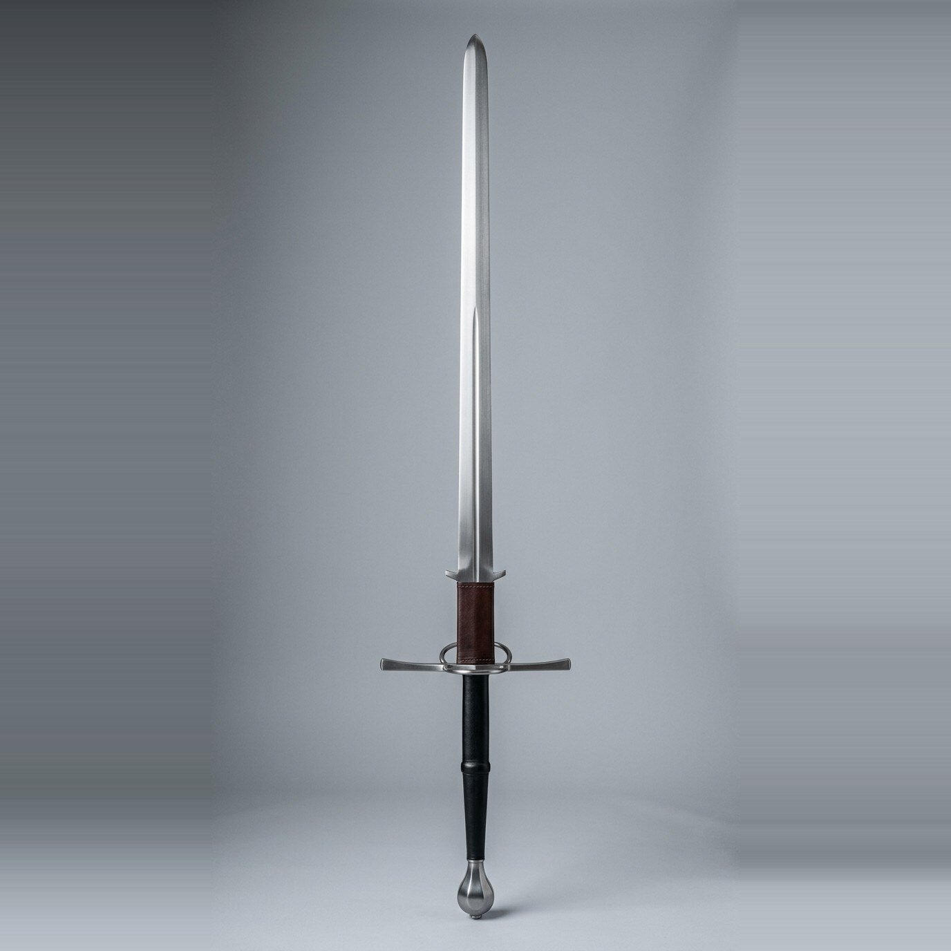 Rundholm montante greatsword Montante greatsword with a straight double edged blade, leather wrapped ricasso, parierhaken hooks, a side ring on the guard and a faceted pear pommel over a long two hand grip against a plain grey studio backdrop