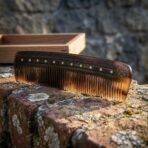 Natural horn beard comb with dotted spine border and vegvisir stave standing on a brick ledge, wooden box behind