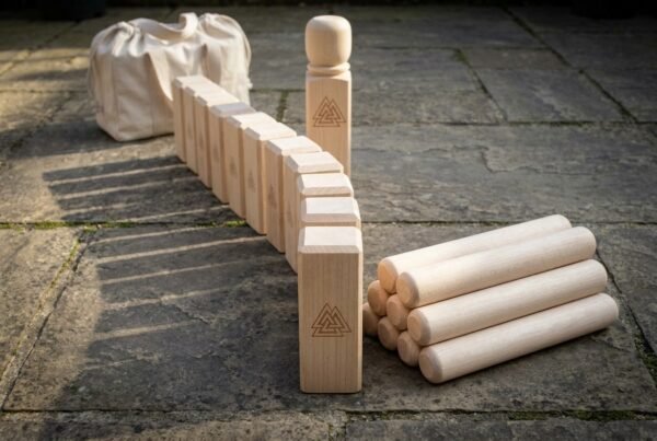 Natural maple kubb lawn game set with Valknut engraved king, row of kubbs, throwing batons and canvas bag on stone paving