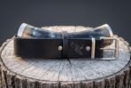 Natural ox drinking horn with polished steel rim and tip bands resting on a raven engraved black leather belt on a stump