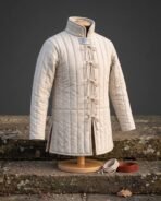 Natural undyed linen padded gambeson with channel quilting, tall standing collar and cord loop lacing on a wooden stand by stone steps